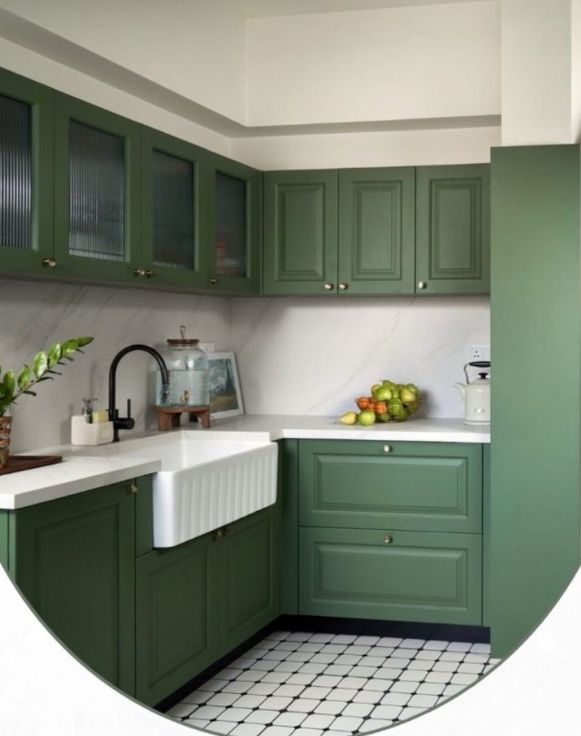 An L-shaped green kitchen with glass-fronted cabinets, a white farmhouse sink and a tiled floor